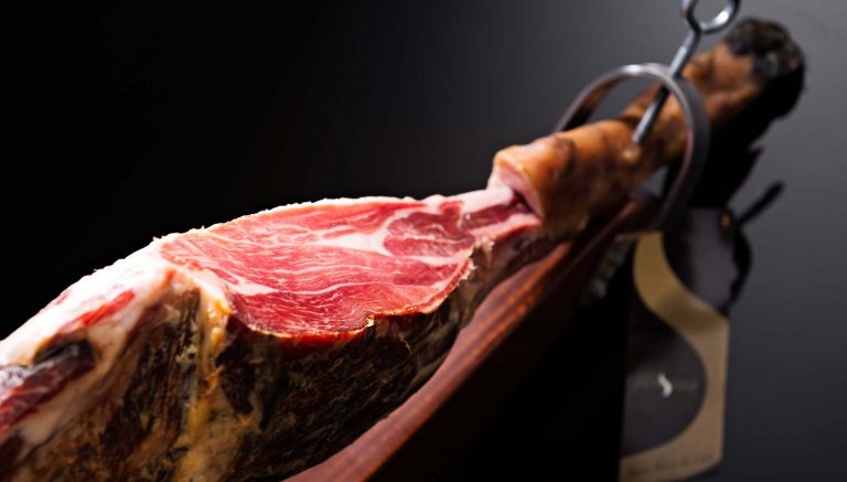 Jamón Ibérico: Todo lo que Necesitas Saber, deliciosa pata de jamón cortado y dispuesto en una elegante tabla de presentación.